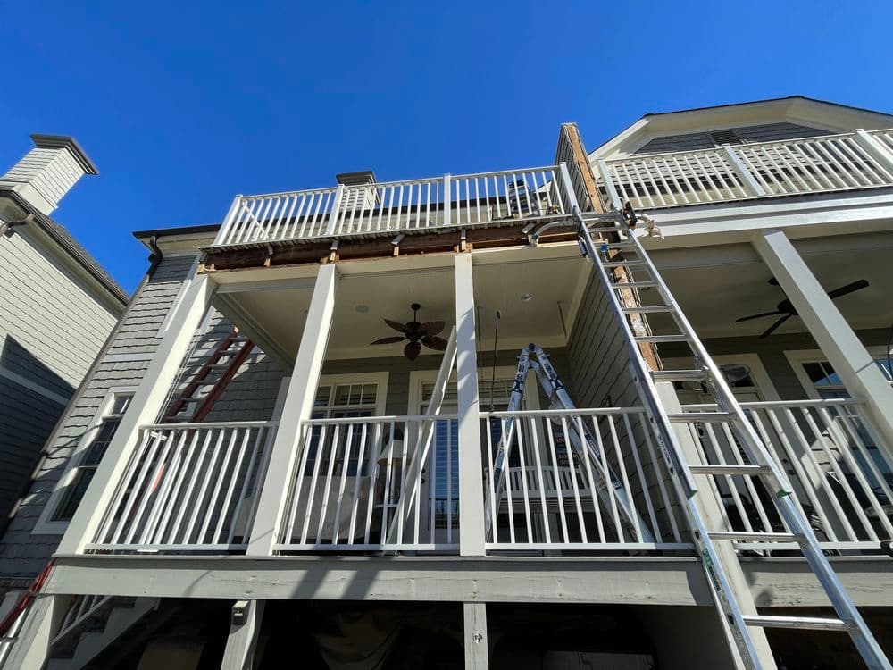 House undergoing renovation with a balcony and ladders against a clear blue sky.