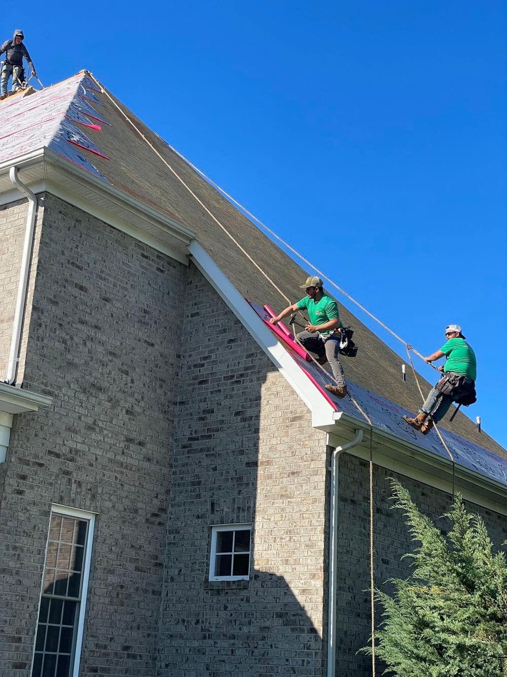 Roofers installing shingles on a residential home under a clear blue sky.