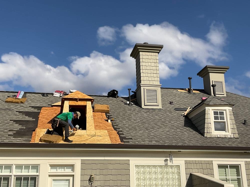 Roofer installing plywood on a house roof under a partly cloudy sky.