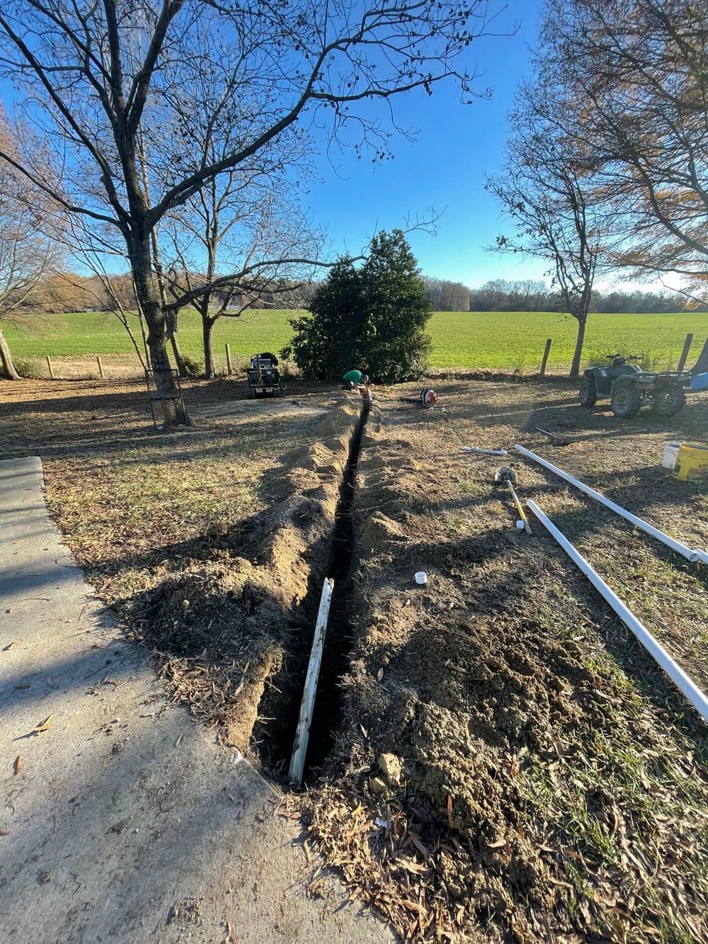 Trenched area for landscaping project with trees and open field in the background.