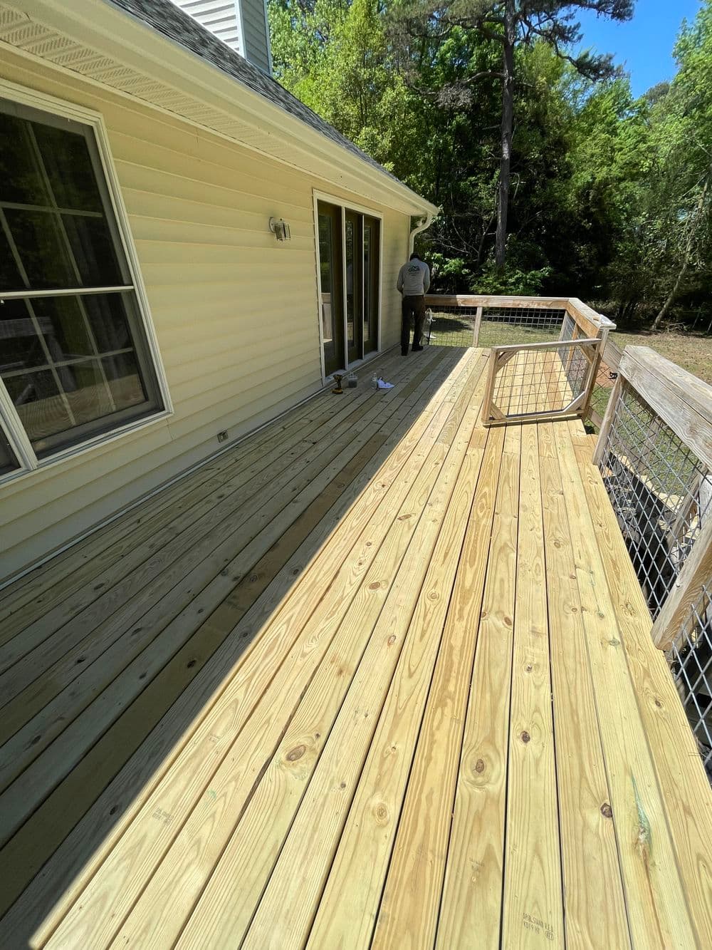 Newly built wooden deck beside a house with a person working in the background.