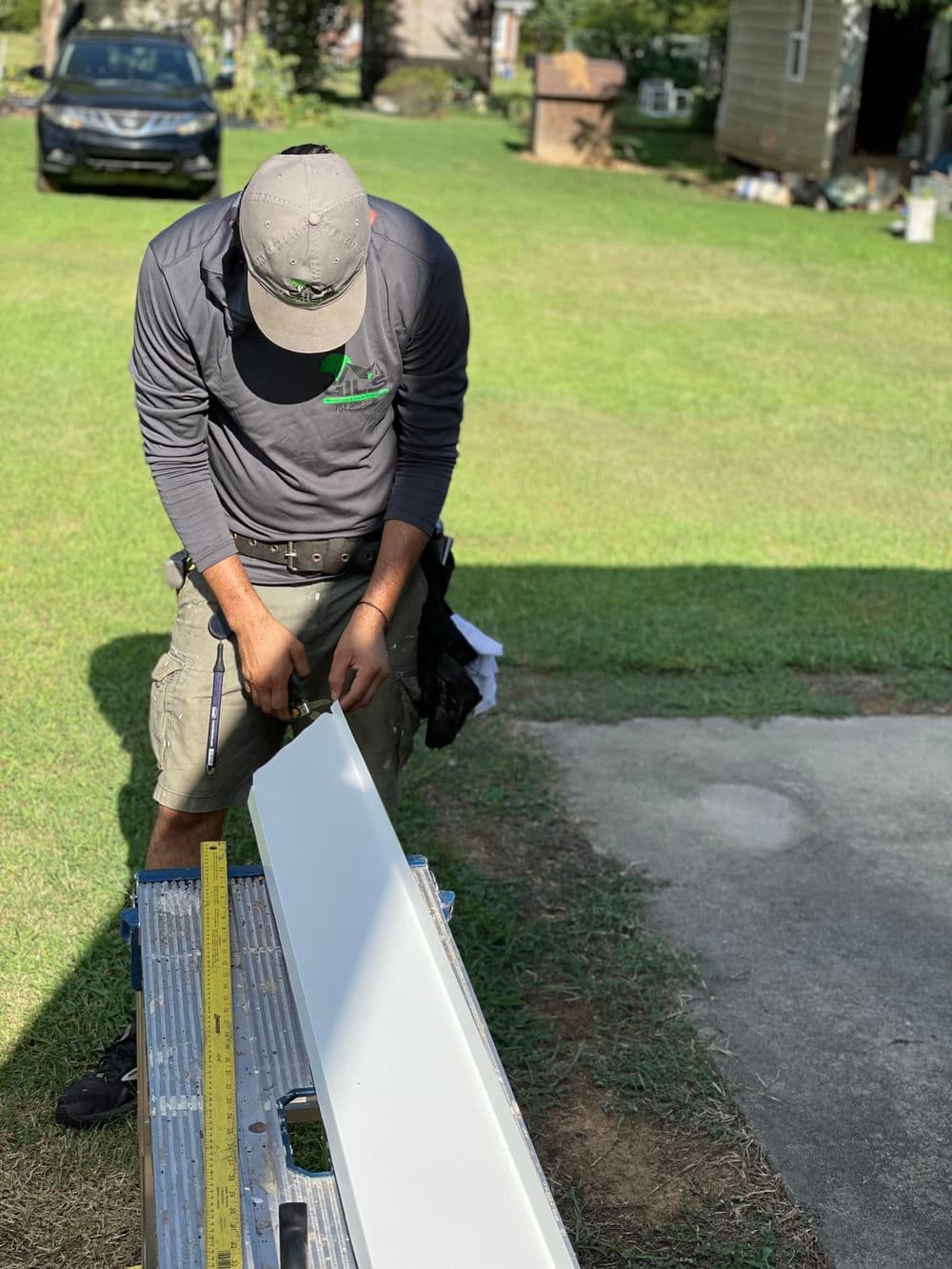 Contractor measuring white siding material on a ladder in a grassy outdoor setting.