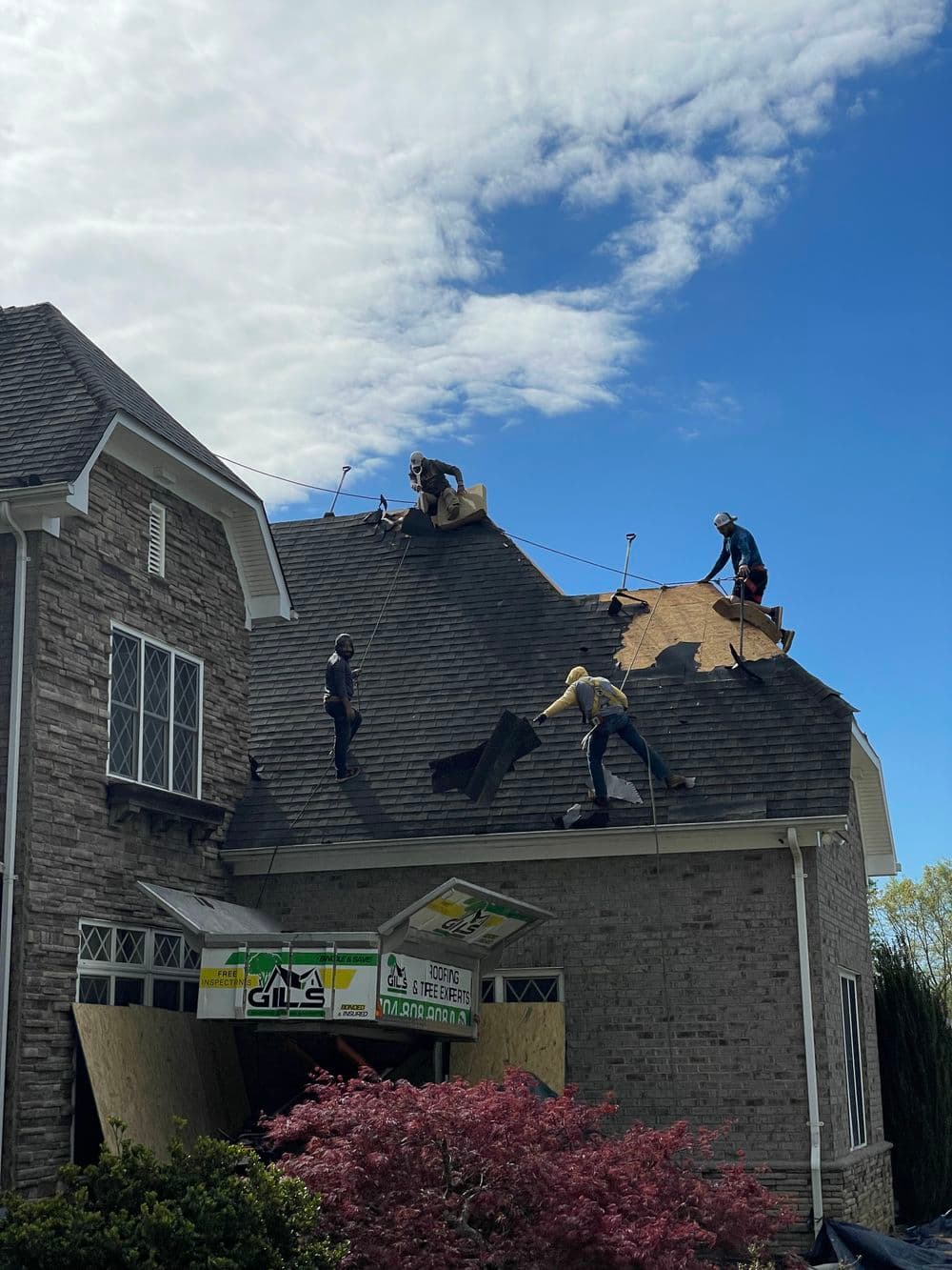 Workers repairing a residential roof with tools and materials on a sunny day.