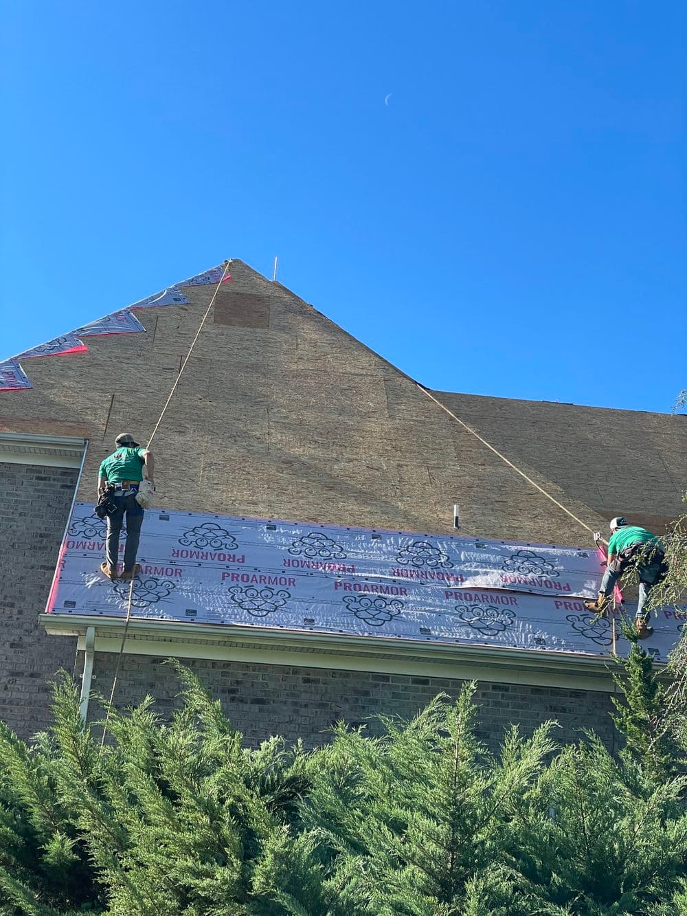 Workers installing roofing underlayment on a house with clear blue sky above.