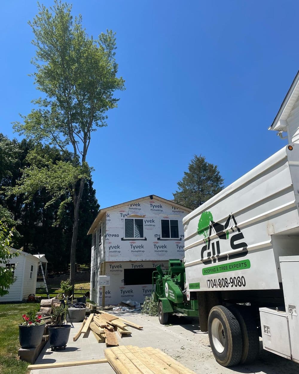 Home renovation with Tyvek wrap, tree removal truck, and construction materials outdoors.