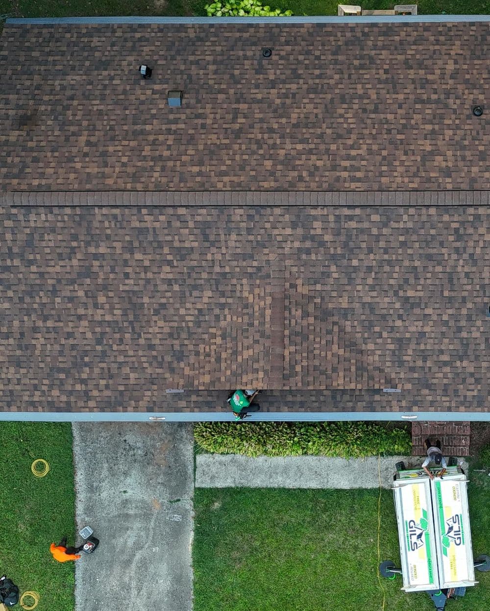 Aerial view of a roof being serviced, with workers and equipment visible on the ground.