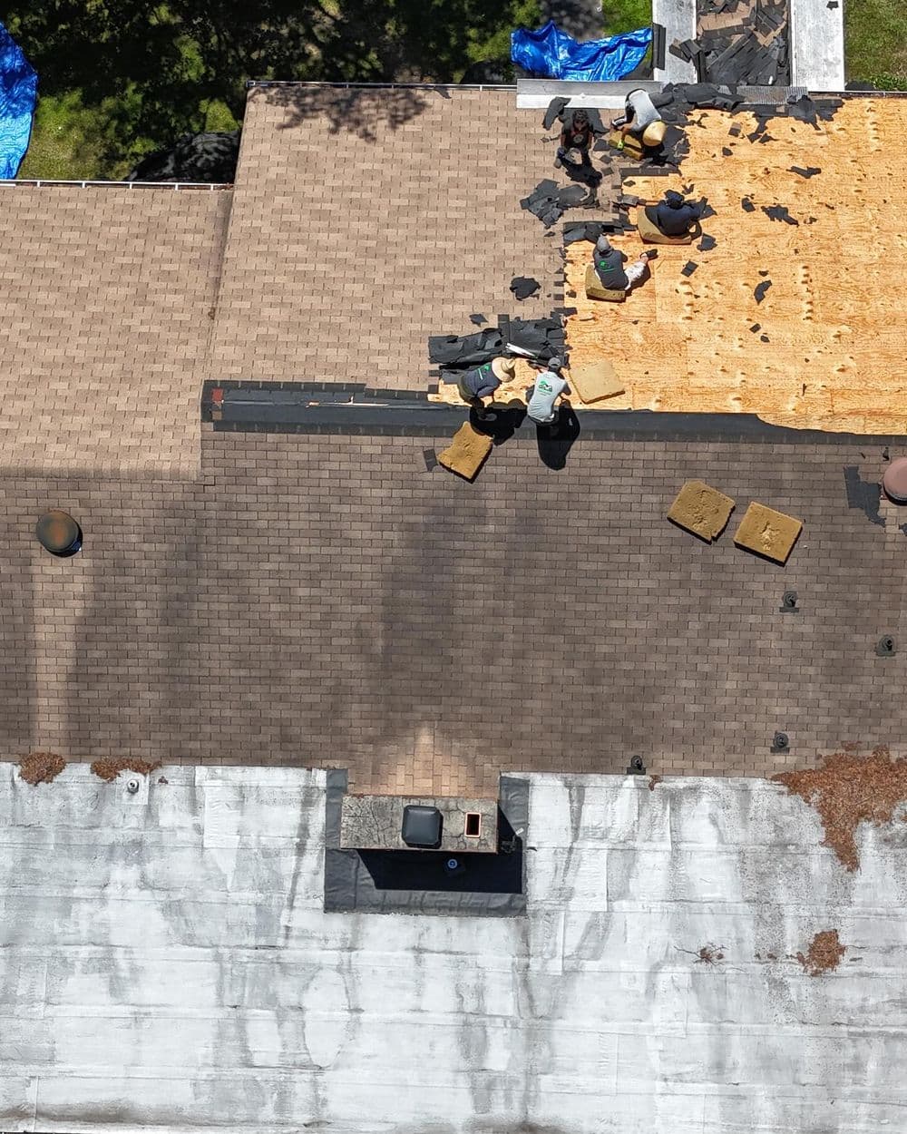 Roof repair project with workers installing new shingles and removing old material.