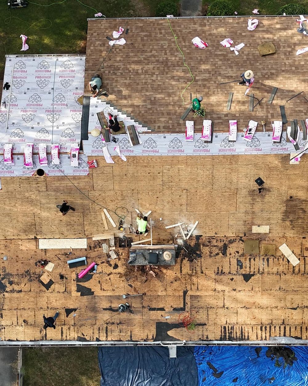 Aerial view of a roof being re-shingled with workers and materials in place.