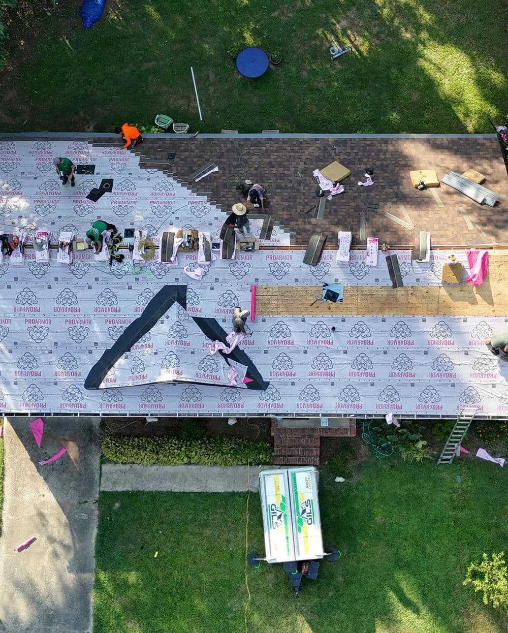 Aerial view of roofing crew installing shingles and underlayment on a residential house.