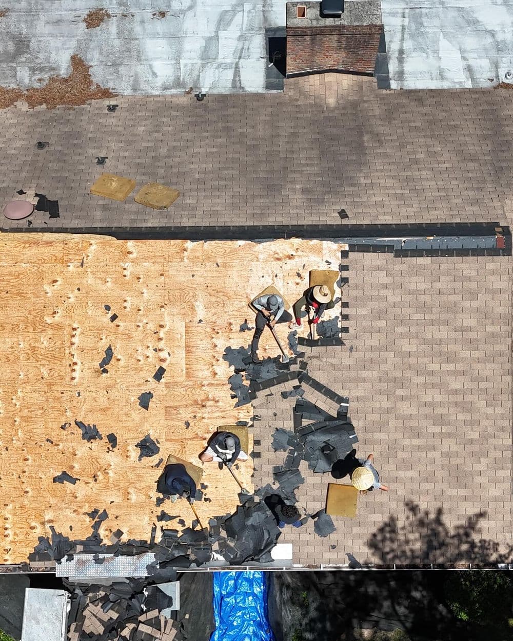 Workers removing old shingles and preparing a roof for new roofing materials.