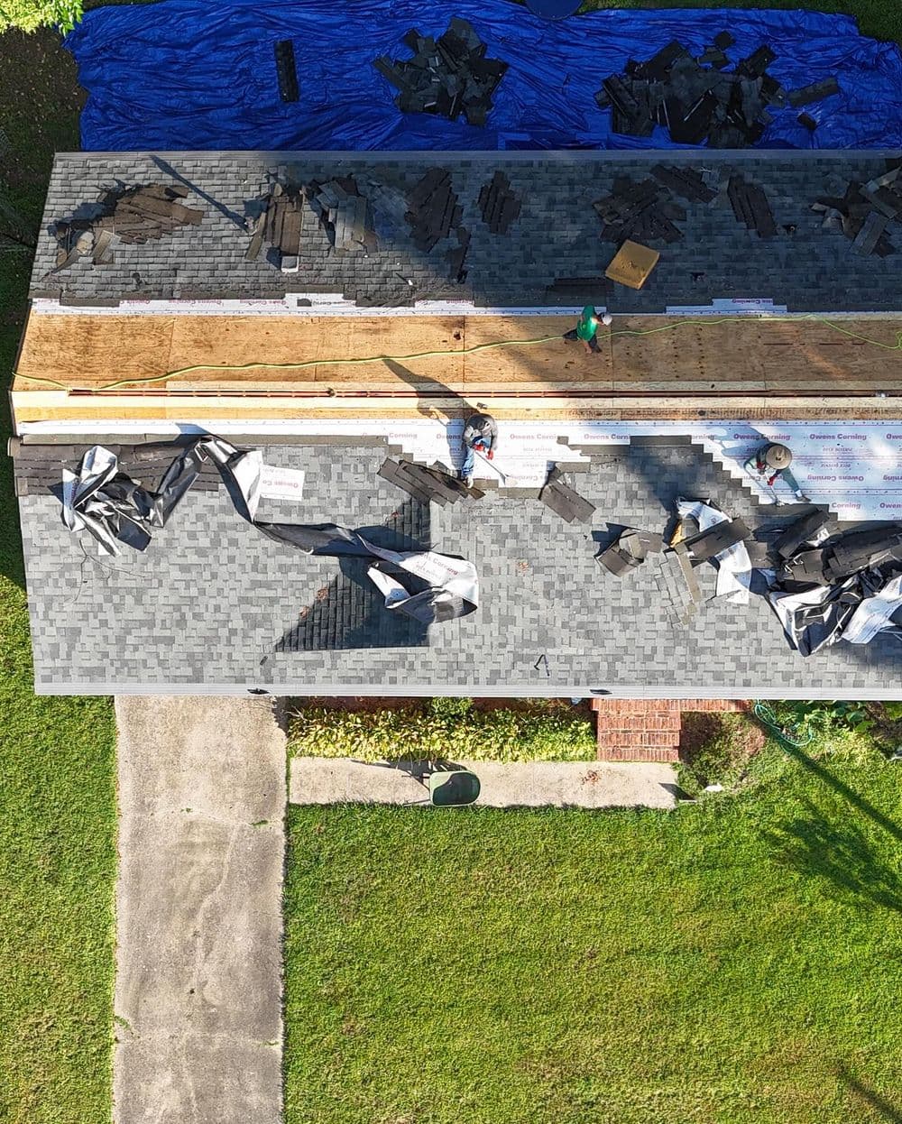 Aerial view of roofers installing shingles on a home's roof with debris and materials.