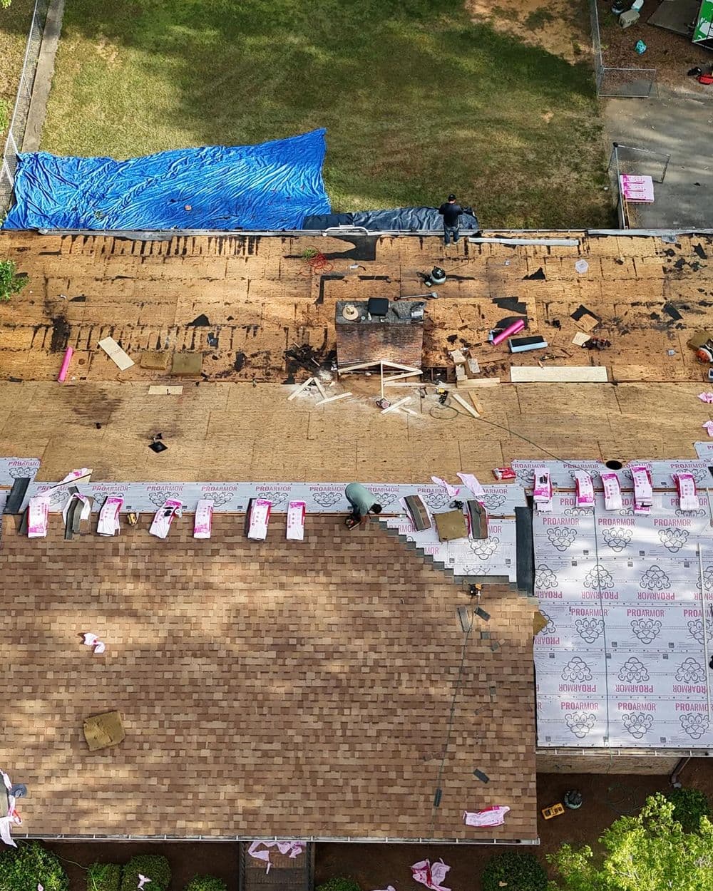 Residential roof under renovation, featuring stripped shingles and workers installing new materials.